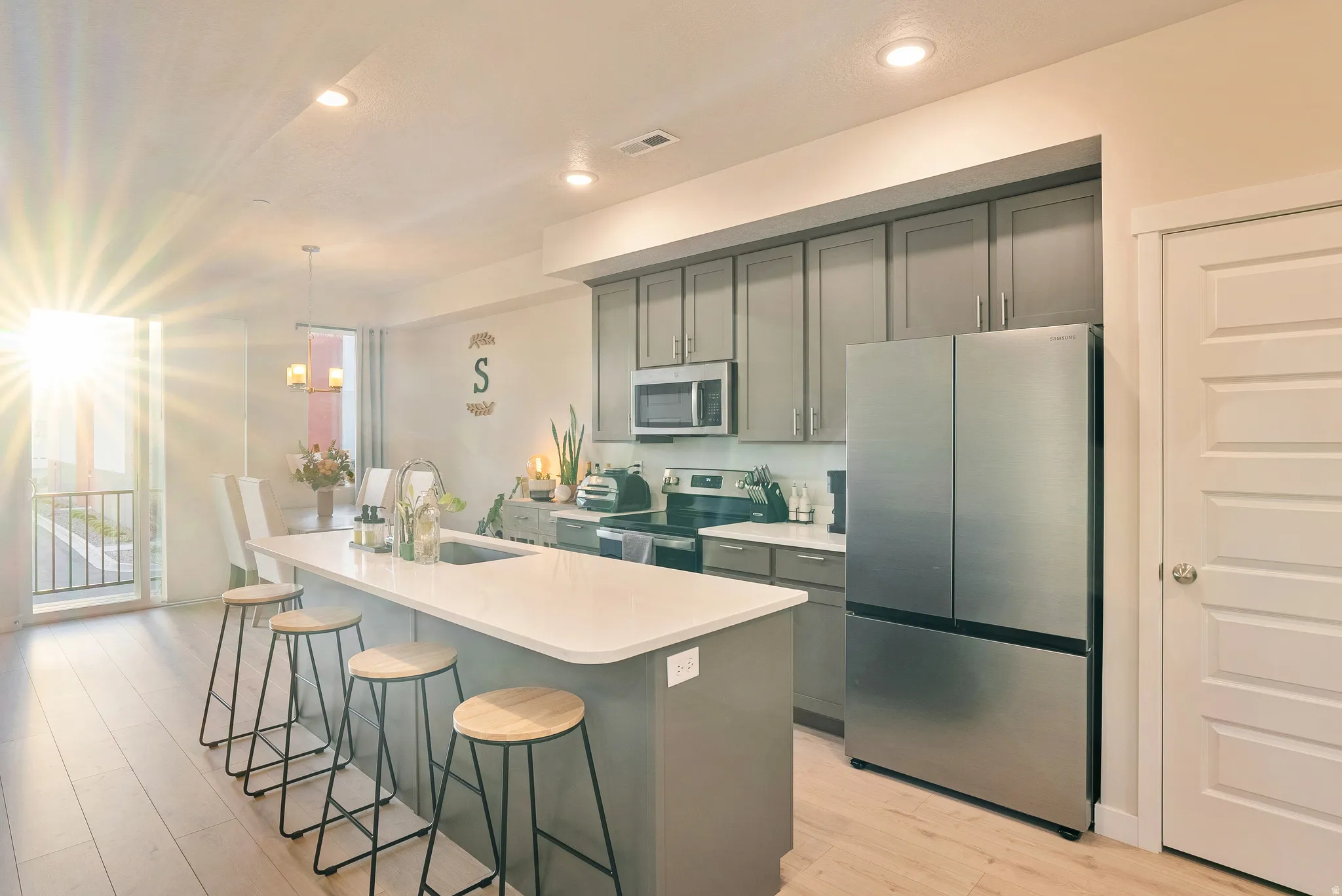 Kitchen with stainless steel appliances, a kitchen breakfast bar, light wood finished floors, a kitchen island with sink, and gray cabinets
