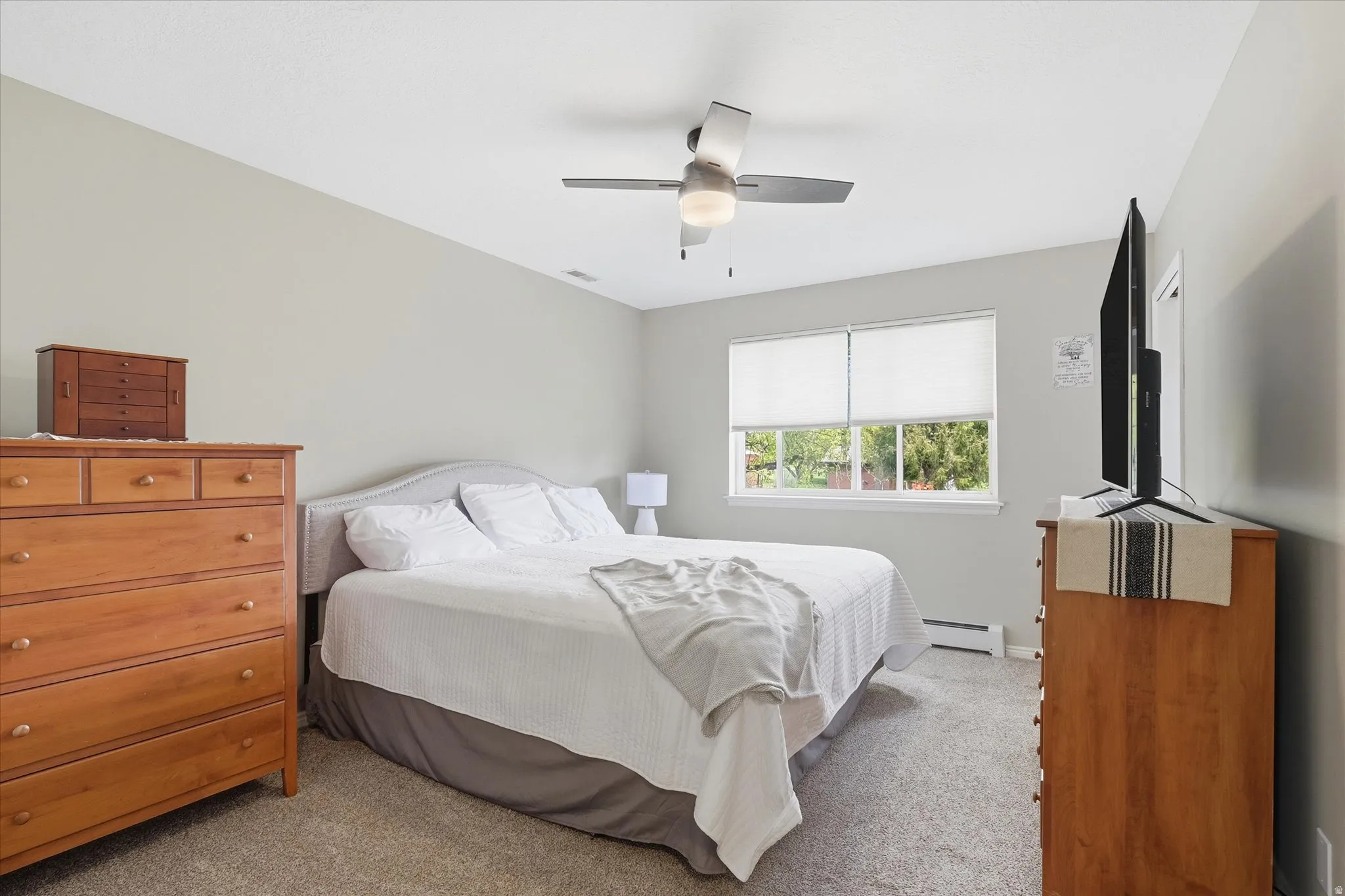 Bedroom featuring light colored carpet, a ceiling fan, and a baseboard heating unit