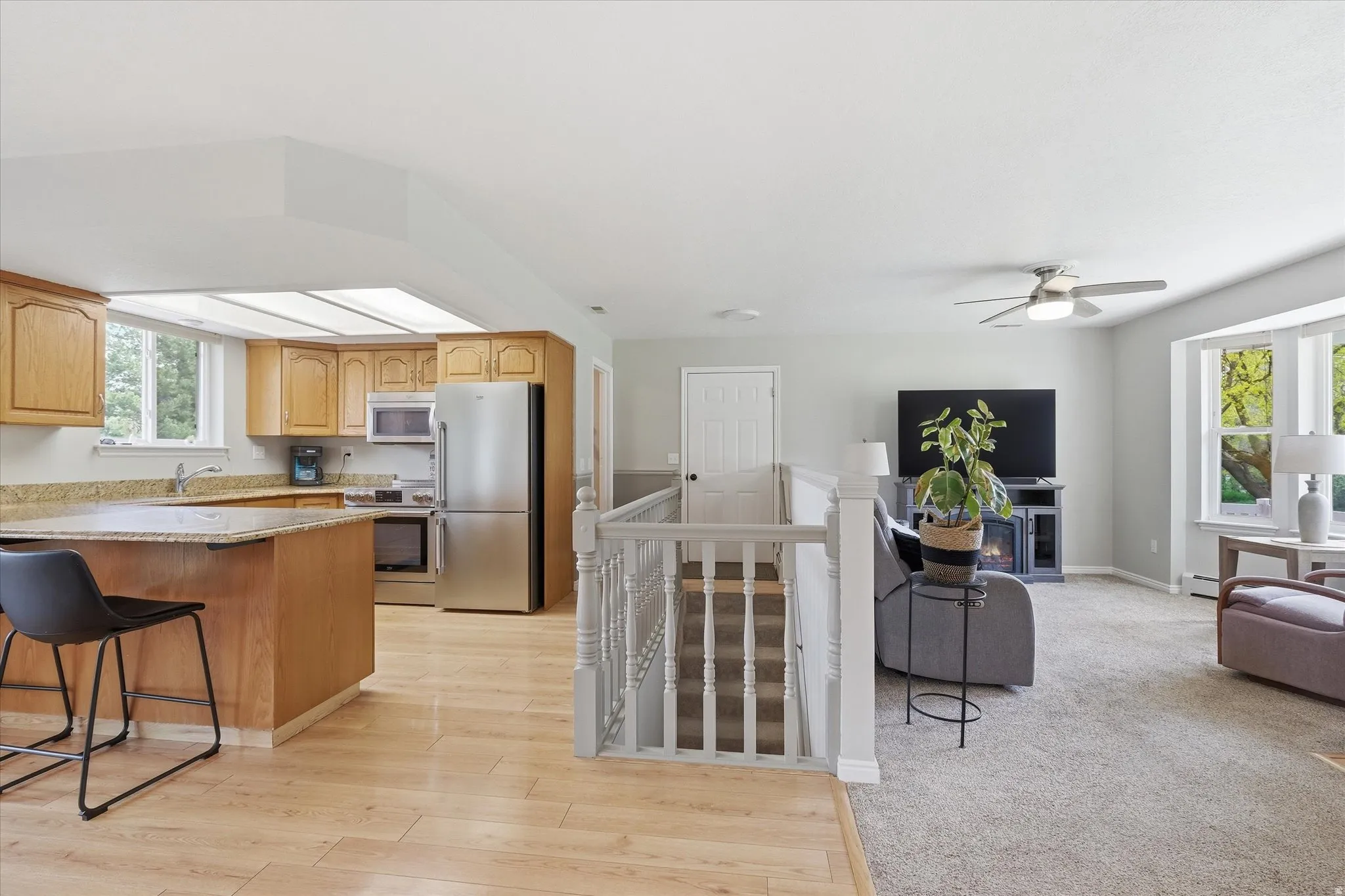 Kitchen with stainless steel appliances, a breakfast bar, light stone counters, light wood finished floors, and ceiling fan