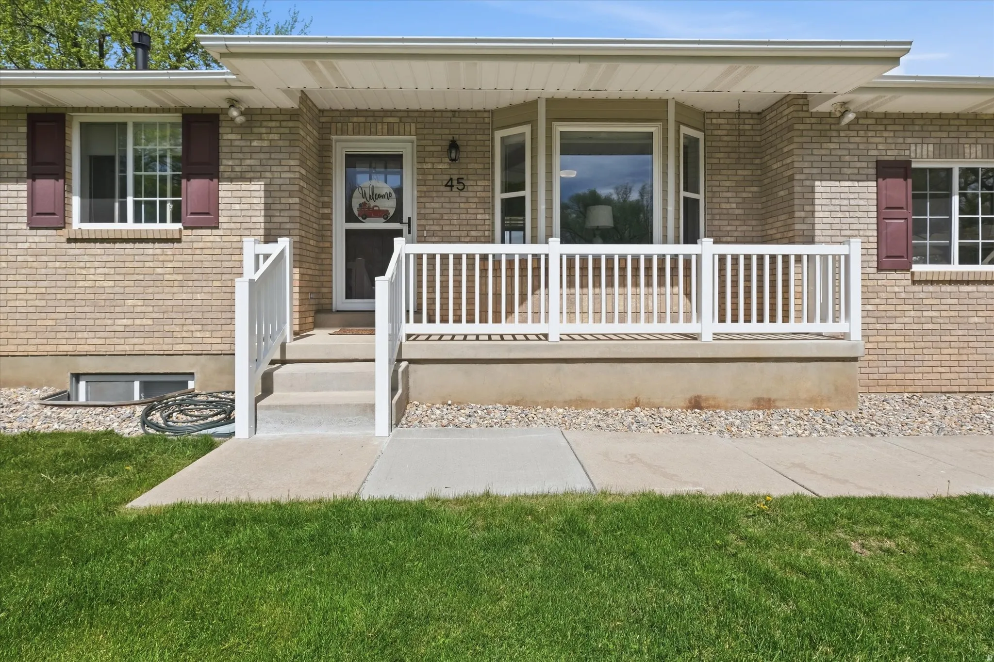 View of exterior entry featuring a porch, brick siding, and a lawn