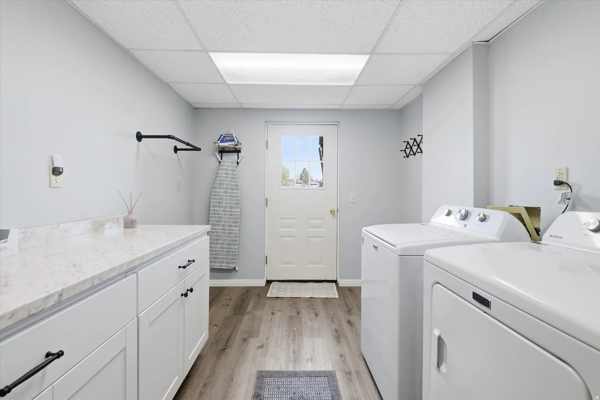 Laundry area with light wood-style flooring, a drop ceiling, separate washer and dryer, and cabinet space
