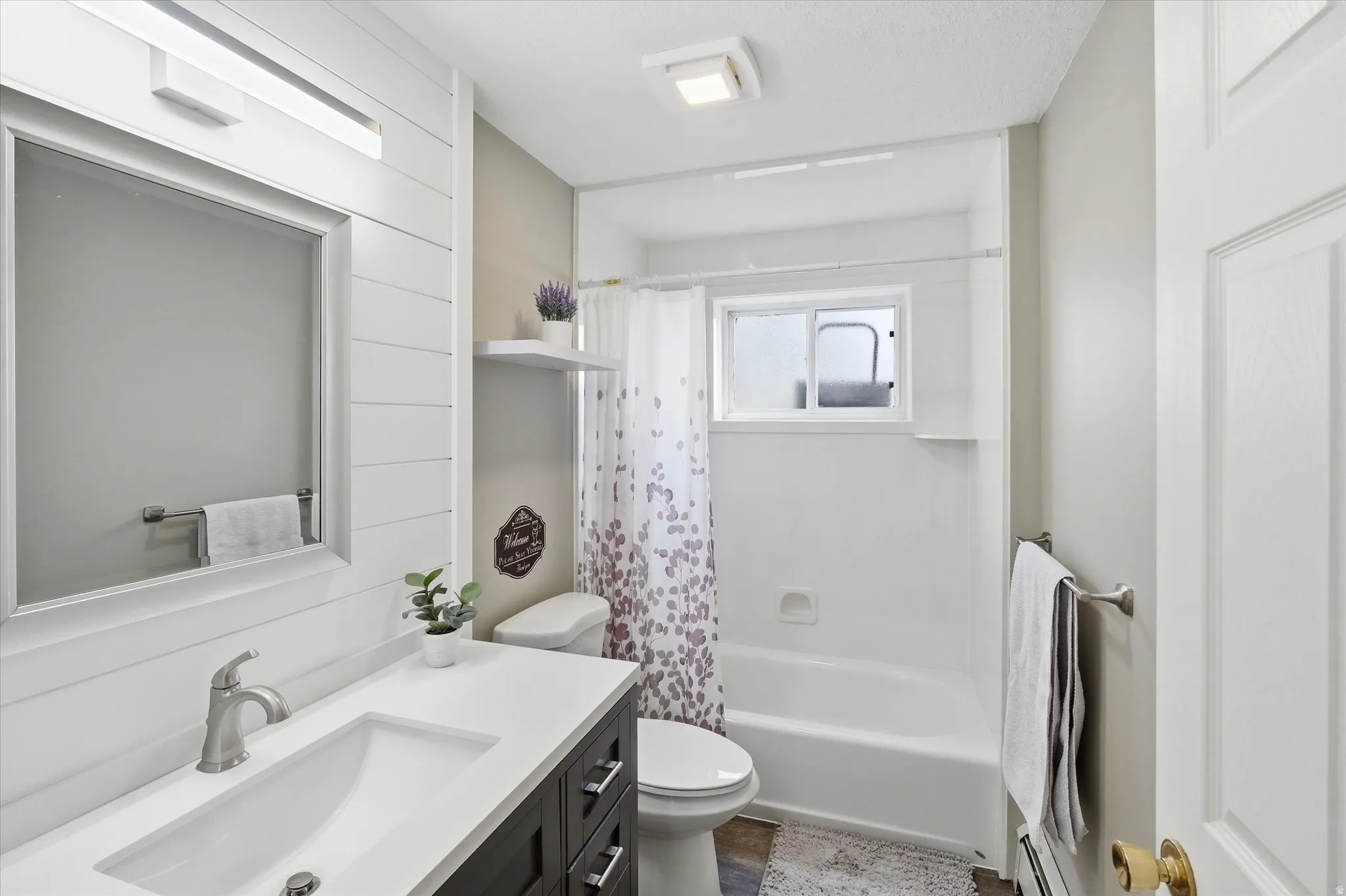 Full bathroom with vanity, shower / bath combo, and a baseboard heating unit