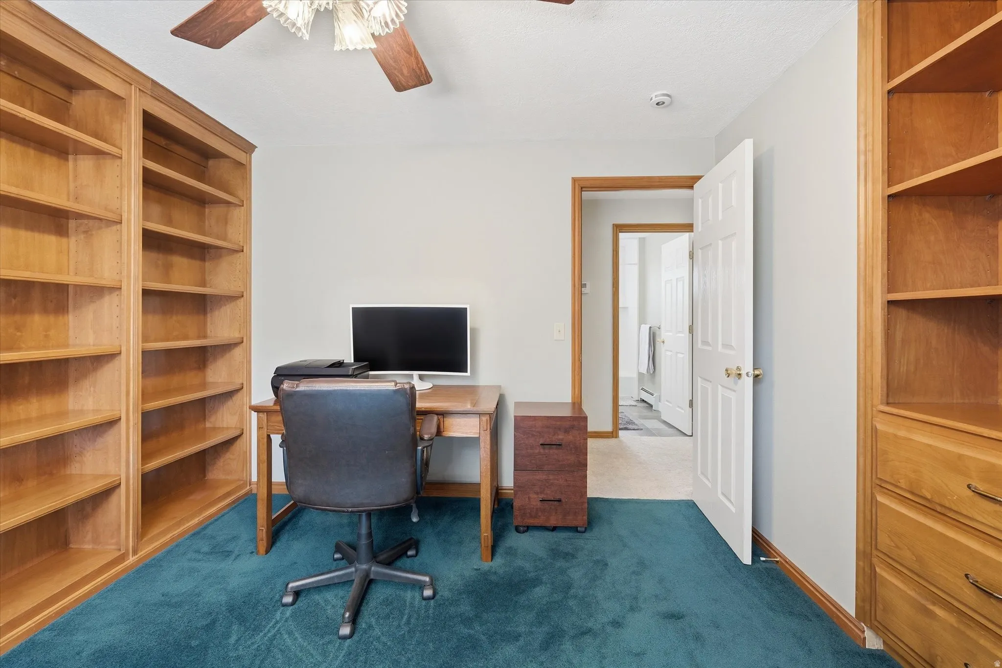 Home office with built in features, dark carpet, and ceiling fan