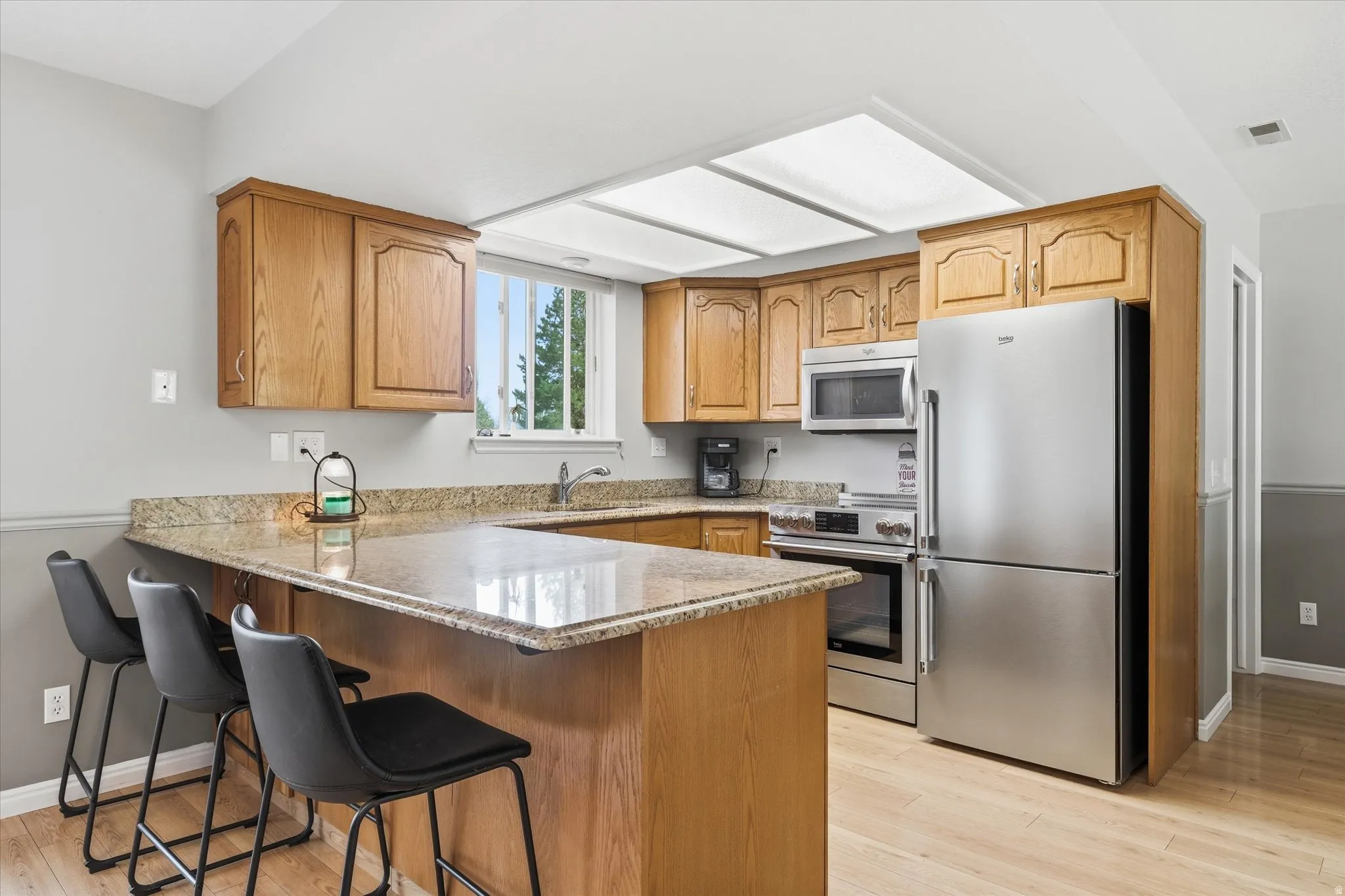 Kitchen featuring stainless steel appliances, light stone counters, light wood-type flooring, a peninsula, and a breakfast bar