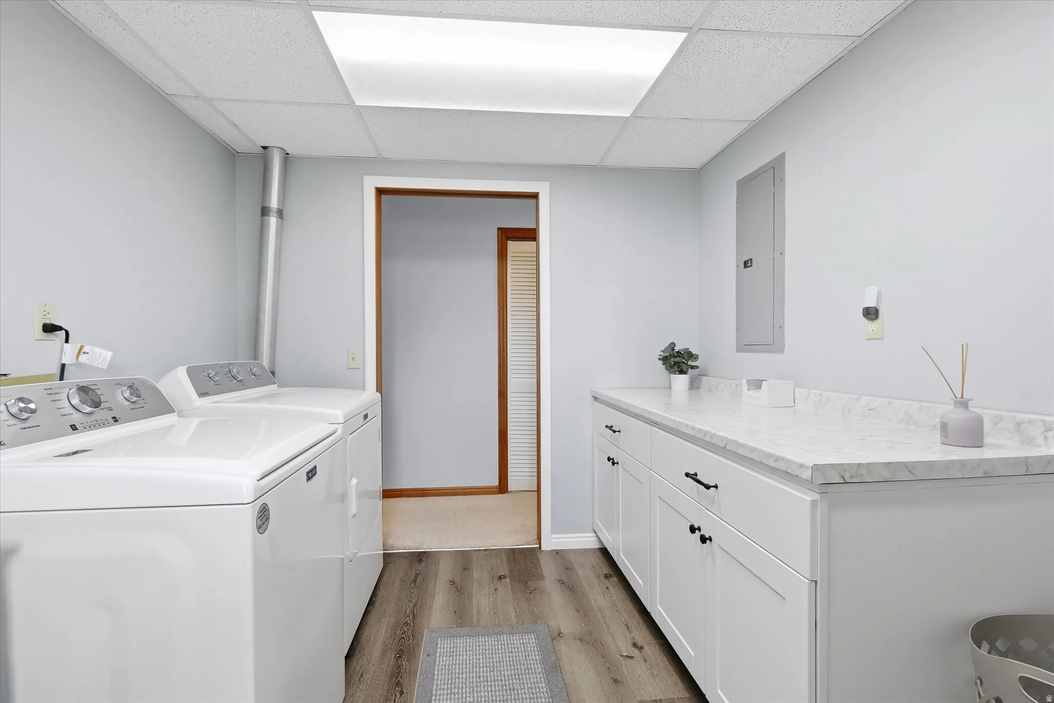 Laundry room featuring light wood-style floors, electric panel, separate washer and dryer, a paneled ceiling, and cabinet space