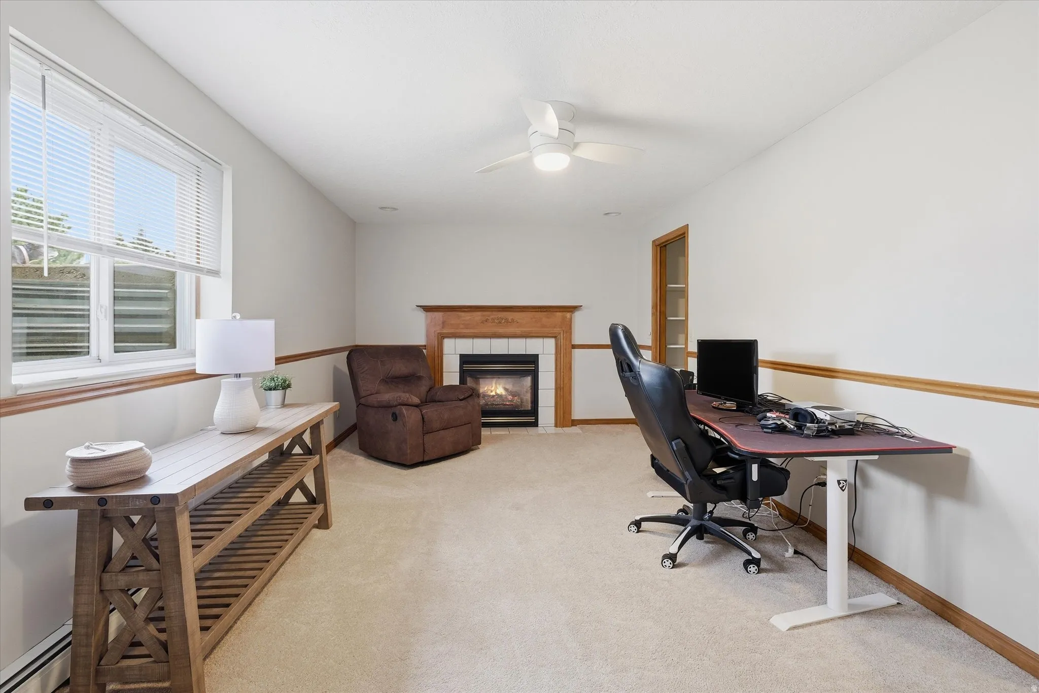 Office with light colored carpet, a fireplace, a baseboard radiator, and ceiling fan