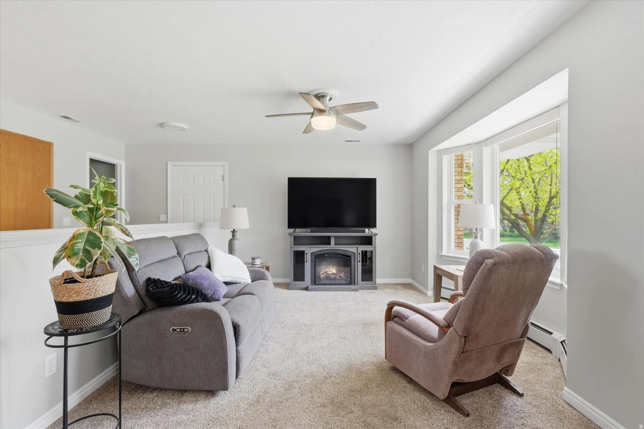 Living room featuring a glass covered fireplace, ceiling fan, light carpet, and baseboard heating