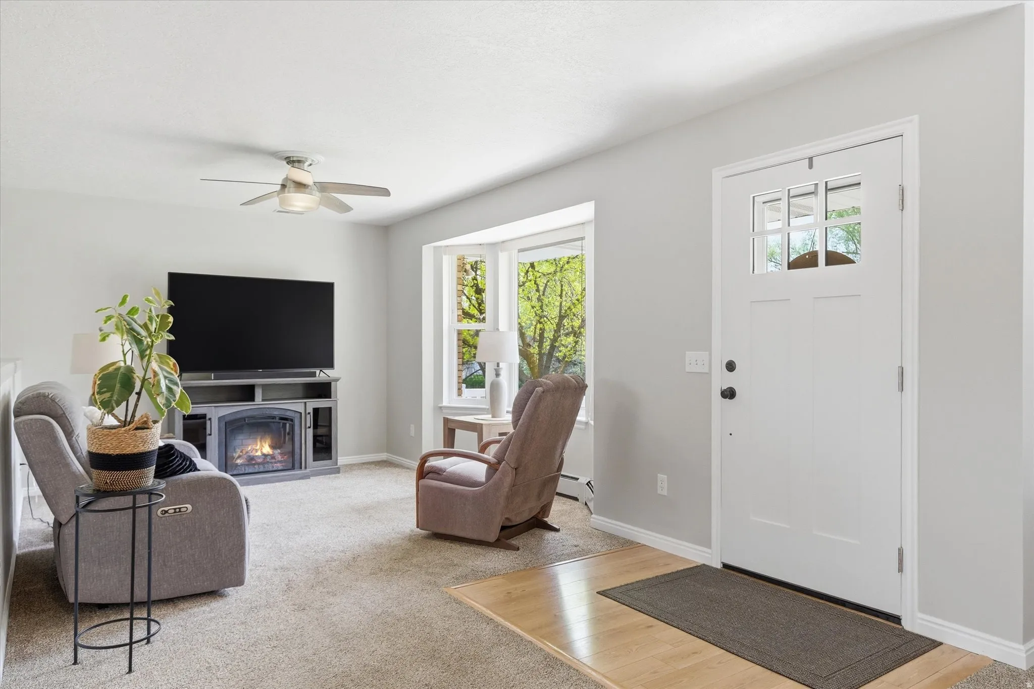 Living area featuring plenty of natural light, a lit fireplace, a ceiling fan, and light colored carpet