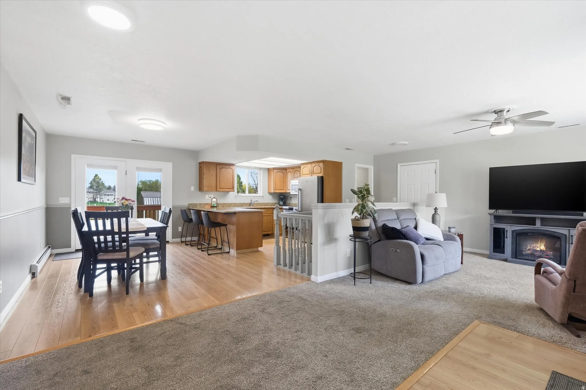 Living room with light wood-type flooring, a fireplace with flush hearth, a baseboard heating unit, and ceiling fan
