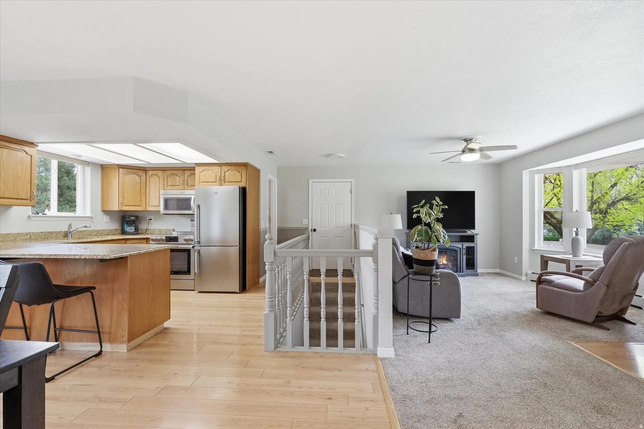 Kitchen with stainless steel appliances, light wood-type flooring, a ceiling fan, light stone counters, and a breakfast bar