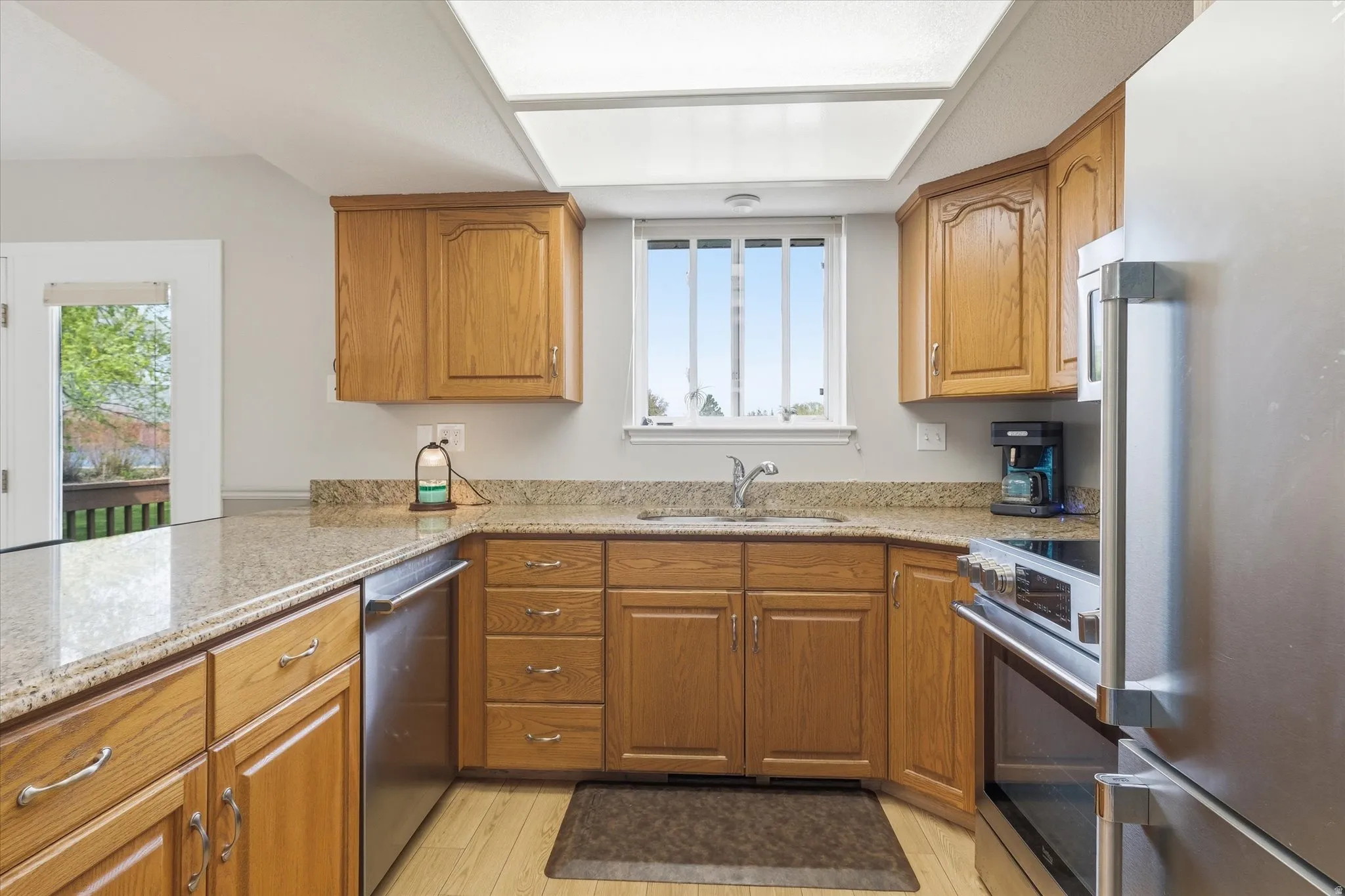 Kitchen with stainless steel appliances, wood finish cabinets, light stone countertops, and light wood finished floors