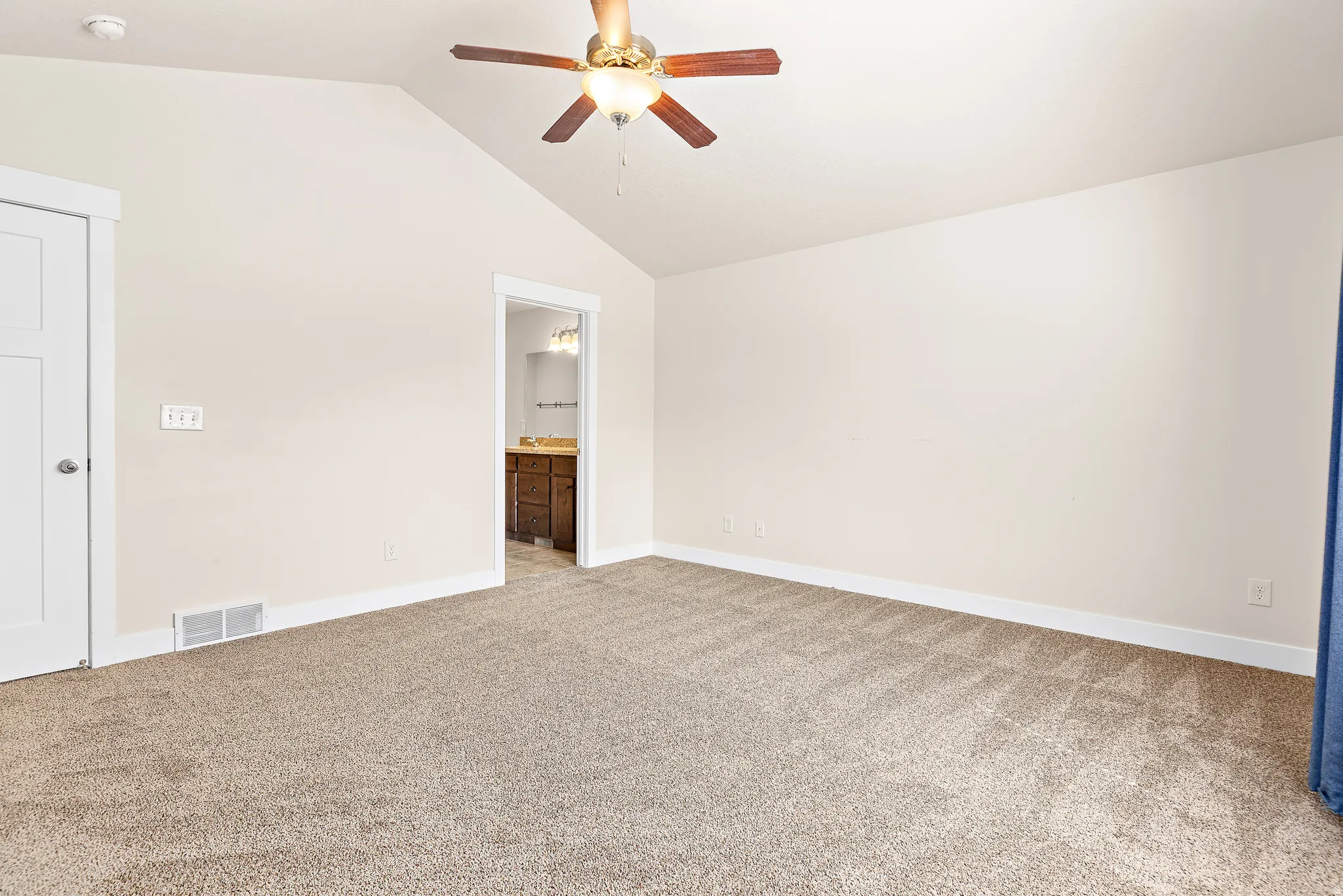 Unfurnished bedroom with light colored carpet, ensuite bathroom, and ceiling fan