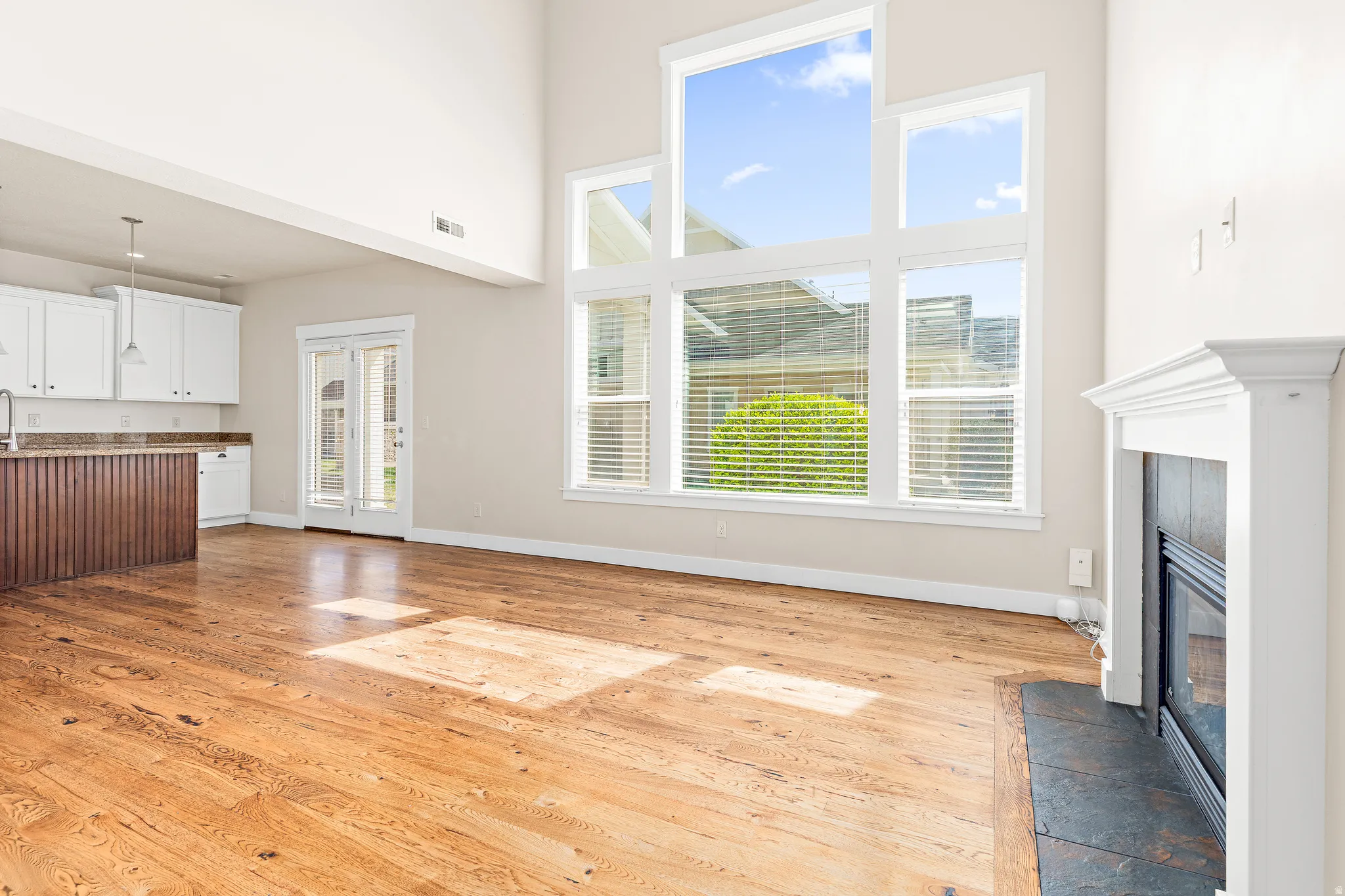 Unfurnished living room with a tiled fireplace, light wood-style flooring, and a high ceiling