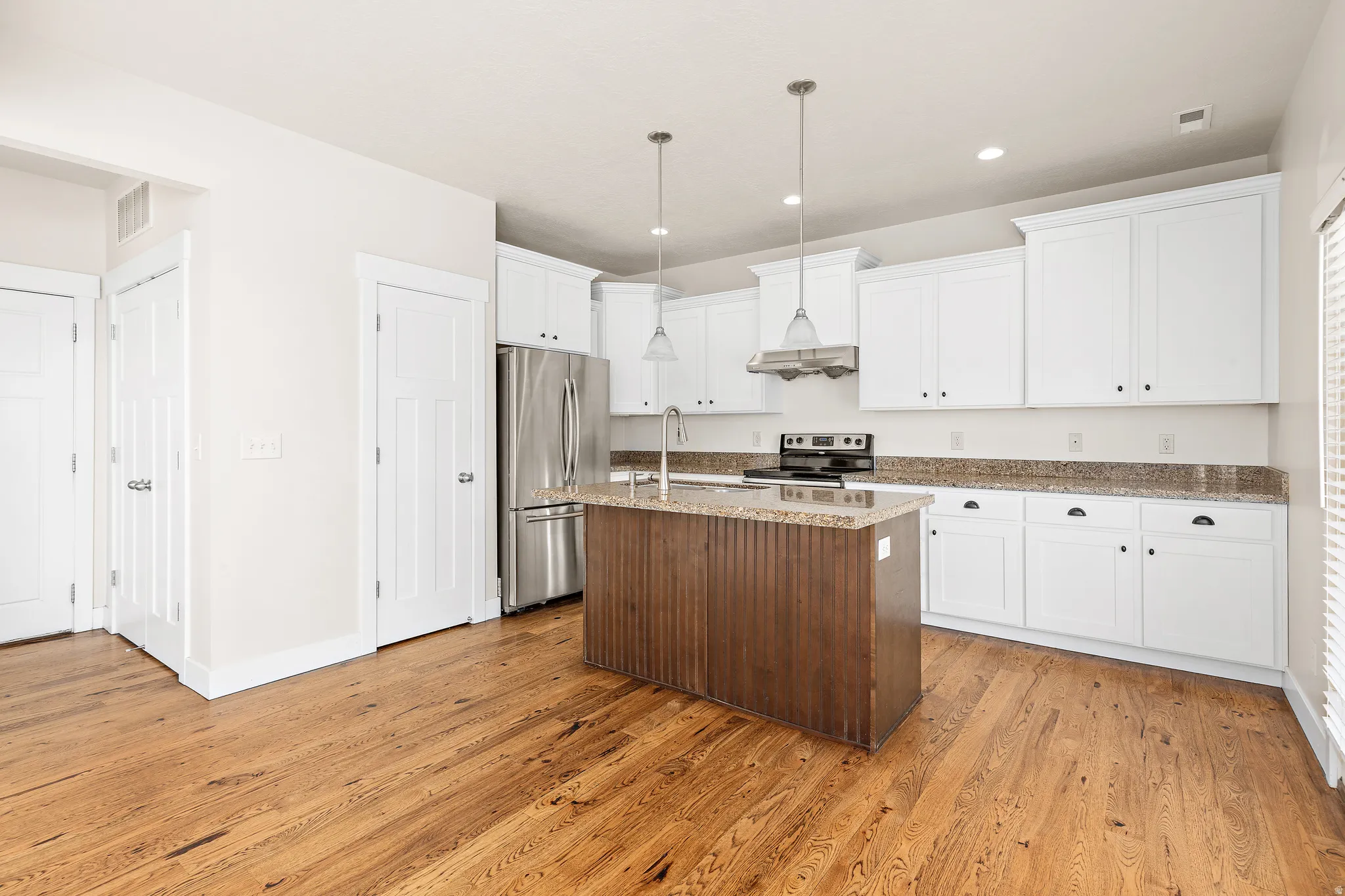 Two tone kitchen with a kitchen island with sink, stainless steel appliances, hanging light fixtures, light stone counters, and light wood-style flooring