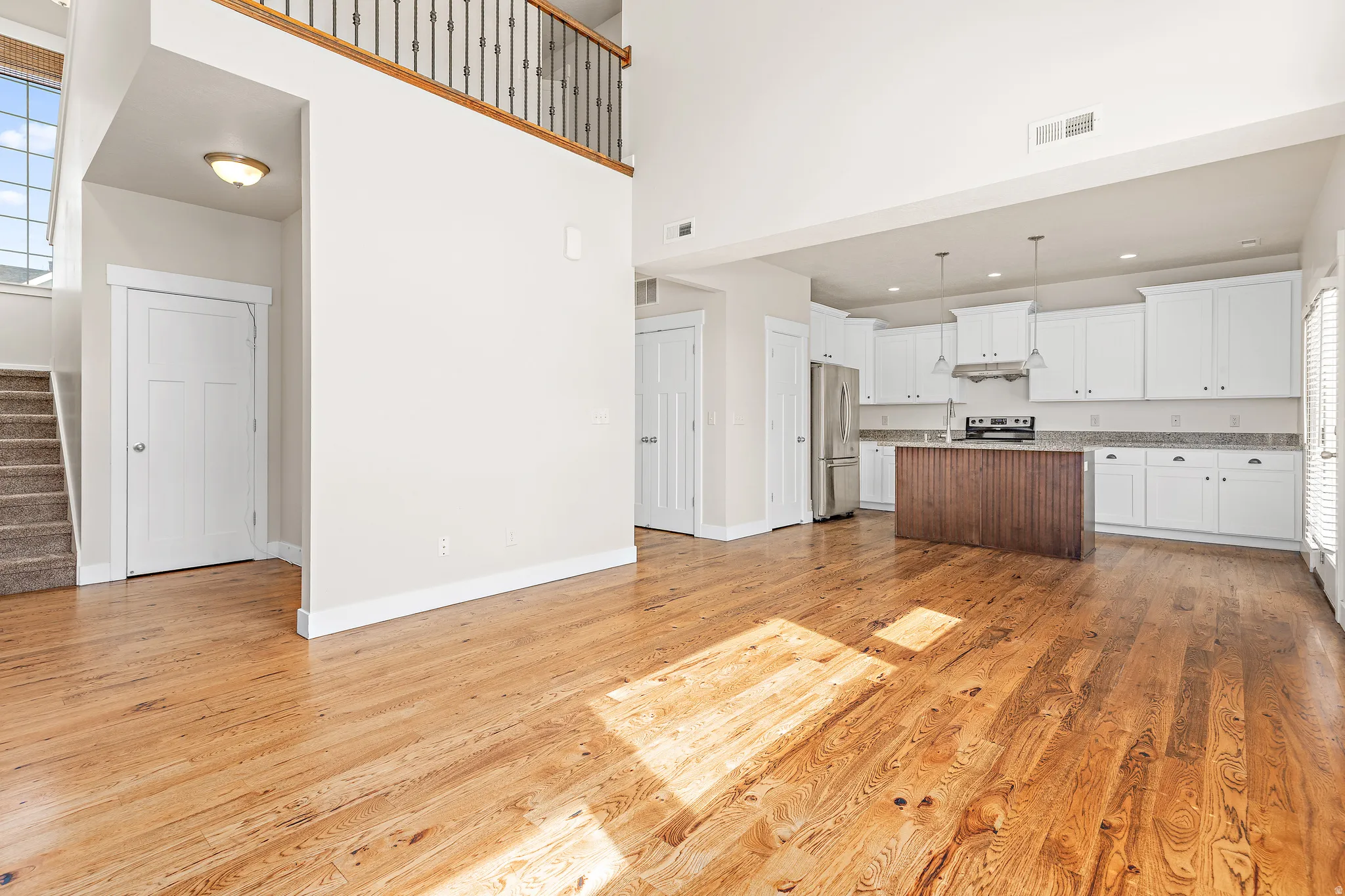 Two tone kitchen featuring a center island, open floor plan, light wood-type flooring, stainless steel appliances, and a high ceiling