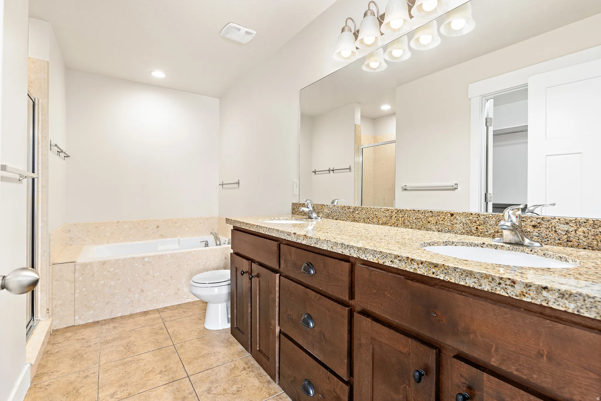 Full bathroom with double vanity, a garden tub, a shower stall, light tile patterned floors, and recessed lighting