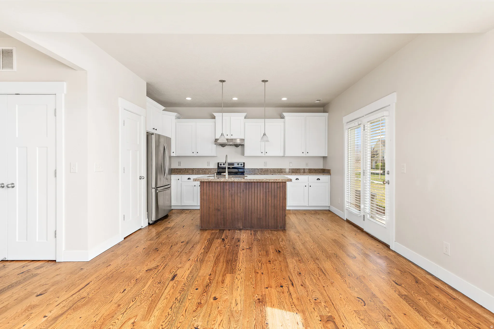 Kitchen featuring white cabinets, decorative light fixtures, light wood-style floors, a kitchen island with sink, and stainless steel appliances