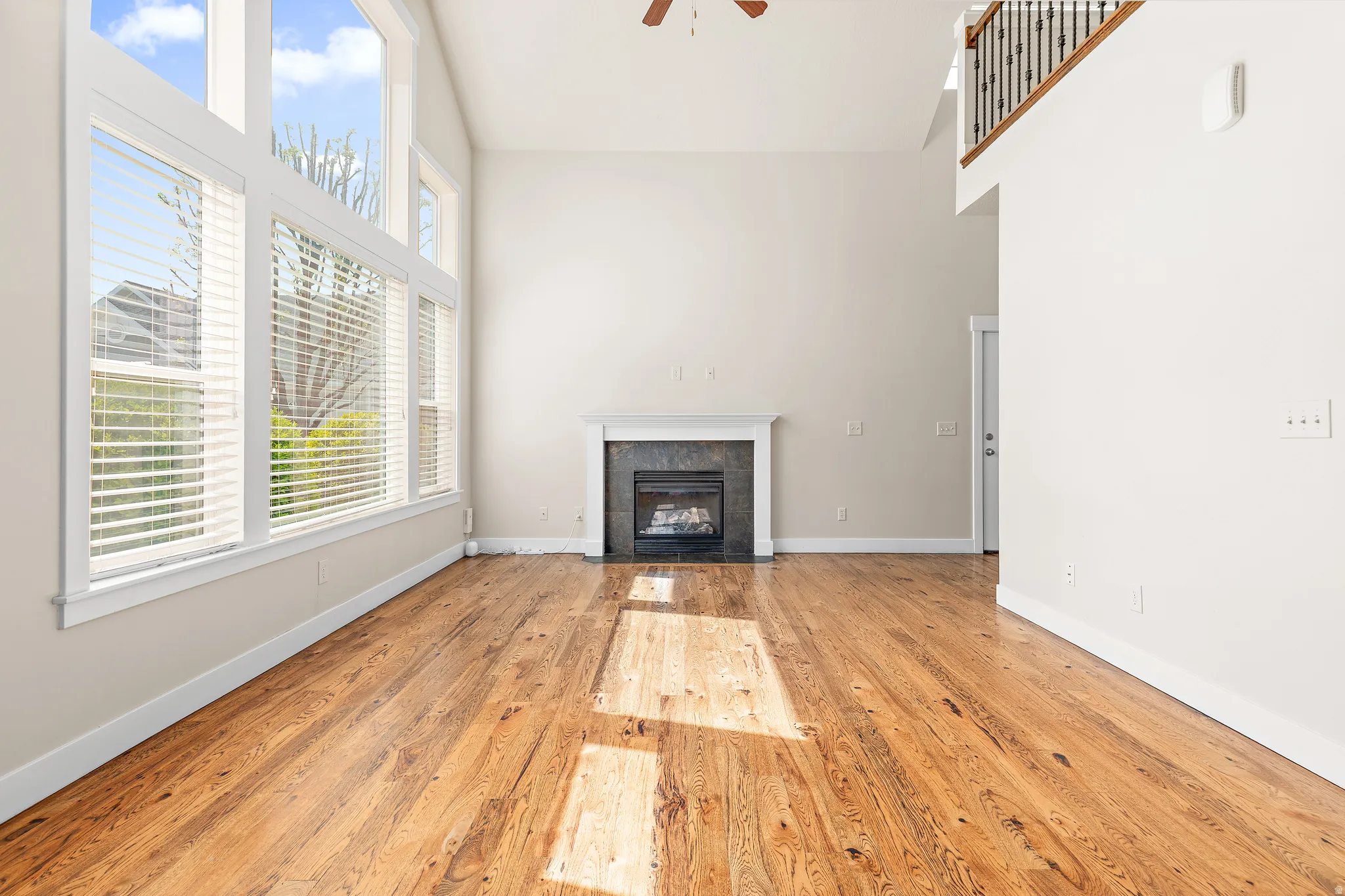 Unfurnished living room with light wood-style flooring, ceiling fan, a tiled fireplace, and vaulted ceiling