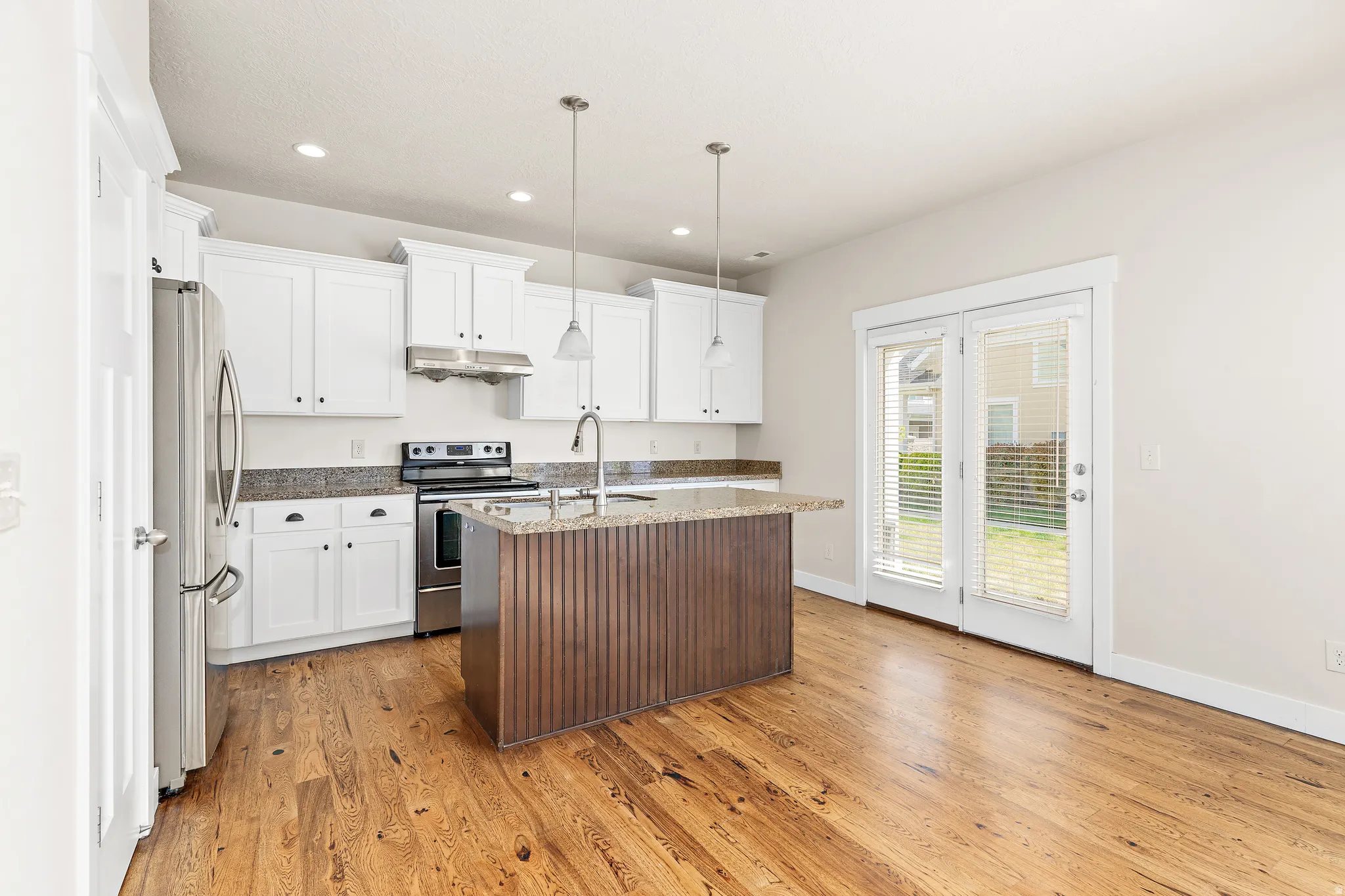 Kitchen featuring stainless steel appliances, a center island with sink, dark stone counters, two tone color scheme, and light wood-type flooring
