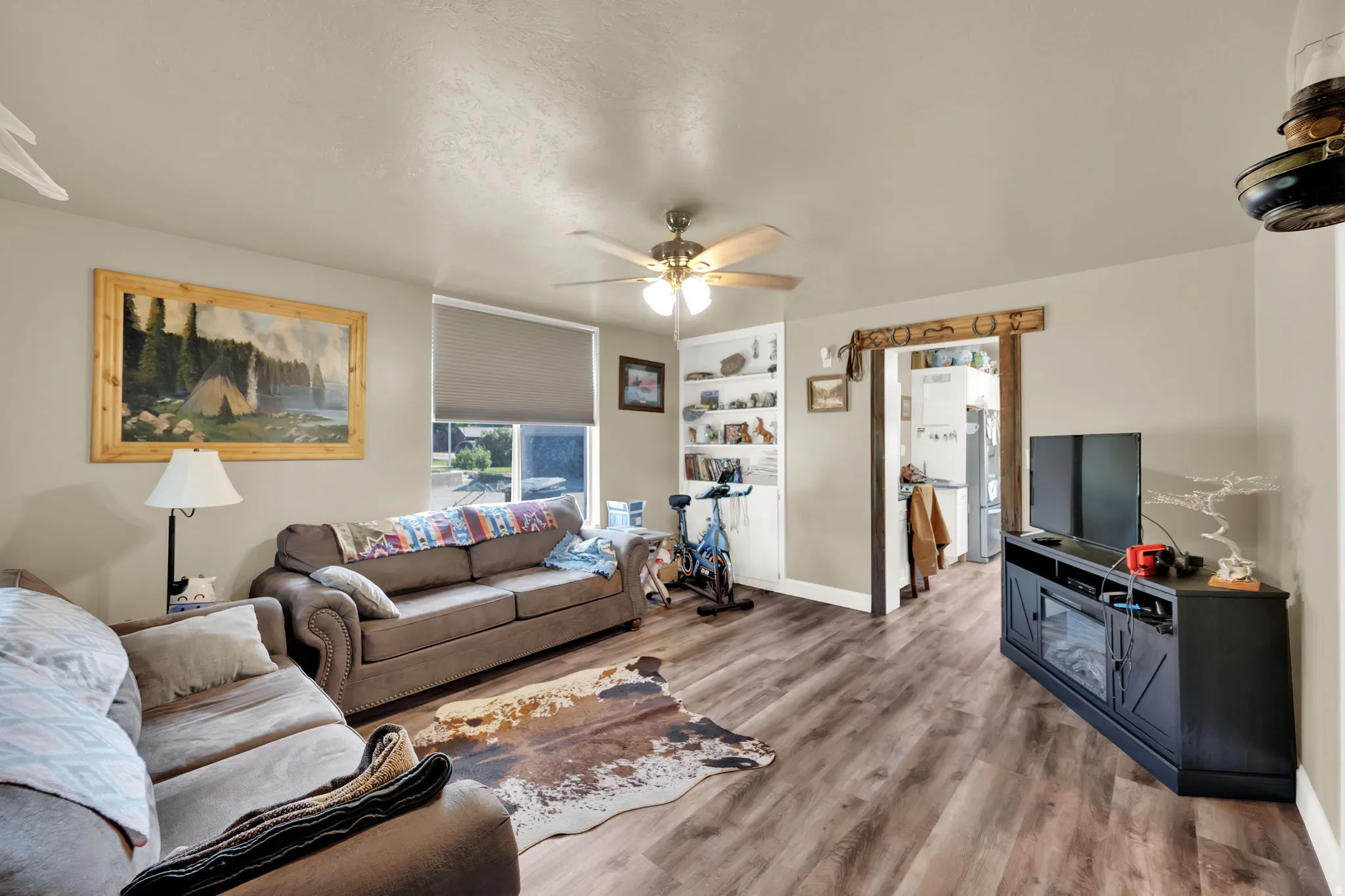 Living room with wood finished floors, a ceiling fan, and built in shelves