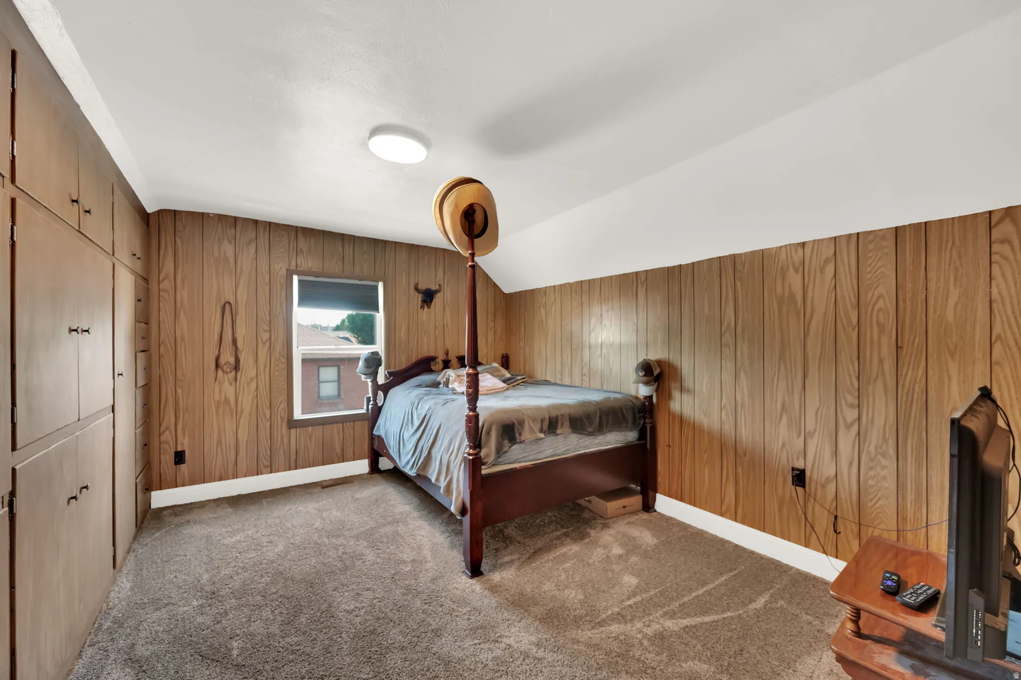 Carpeted bedroom featuring a closet, wood walls, and vaulted ceiling