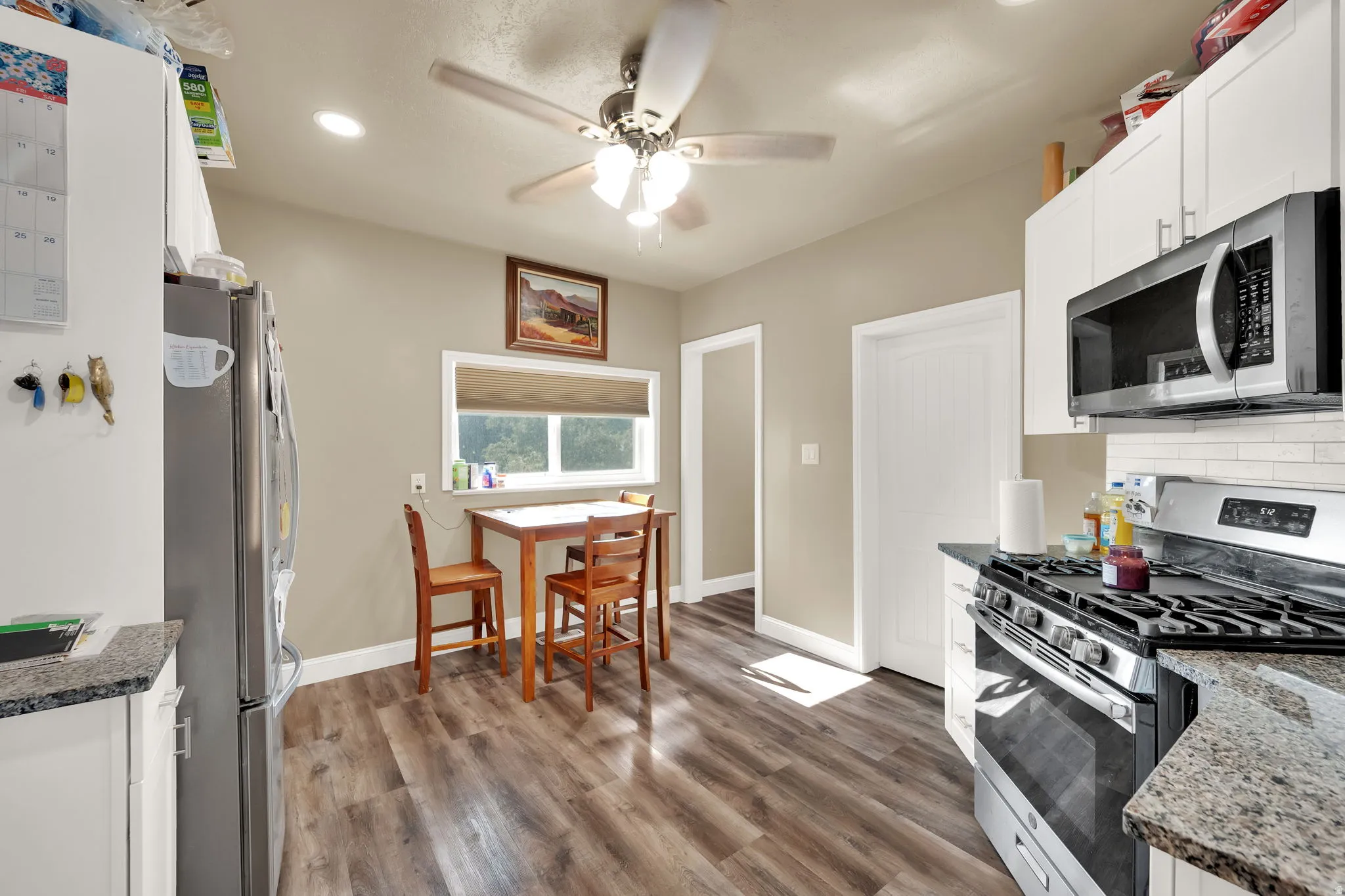 Kitchen with stainless steel appliances, white cabinetry, dark stone counters, dark wood finished floors, and recessed lighting
