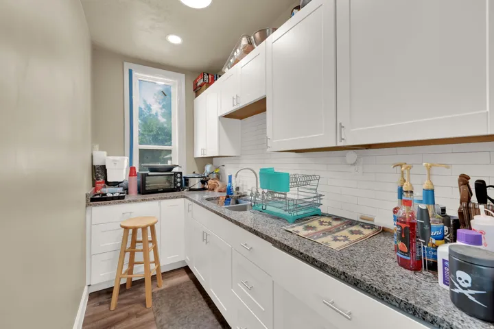 Kitchen with white cabinets, dark wood-style floors, light stone countertops, recessed lighting, and decorative backsplash