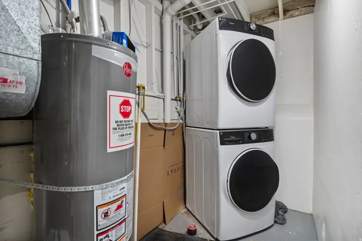 Laundry area with water heater, concrete floors, and stacked washer / drying machine