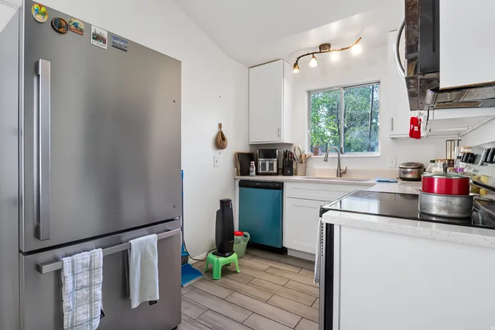 Kitchen featuring freestanding refrigerator, light countertops, white cabinetry, dishwashing machine, and lofted ceiling