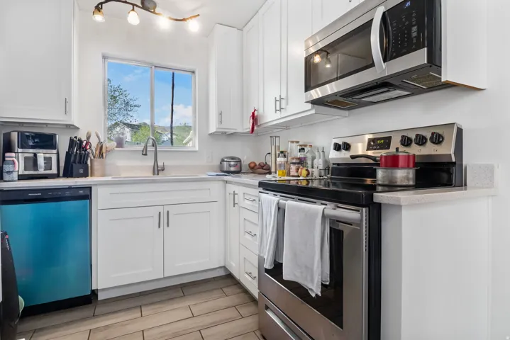 Kitchen featuring stainless steel appliances, white cabinetry, and light stone countertops