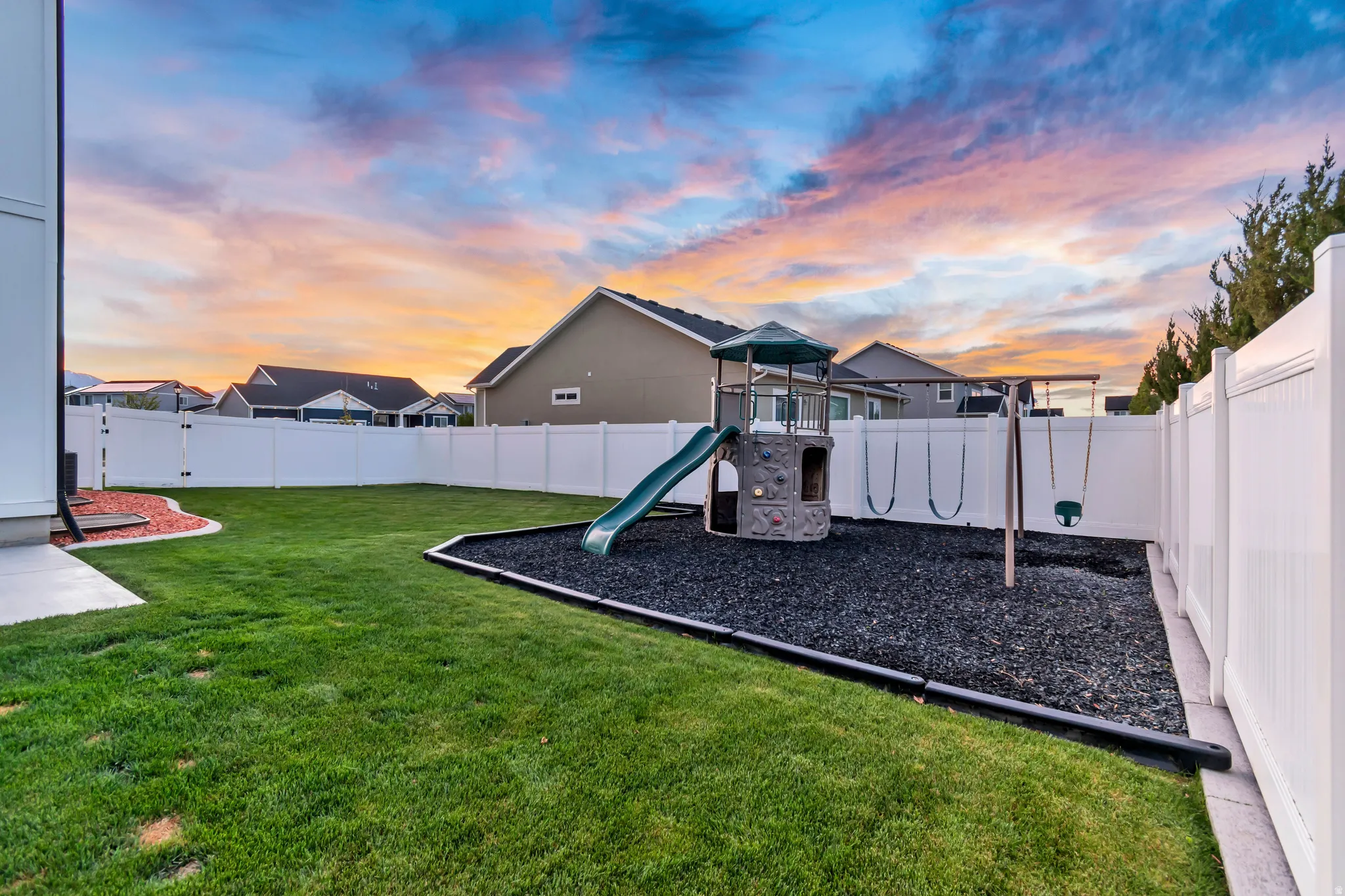 Fenced backyard featuring a playground and grassy area