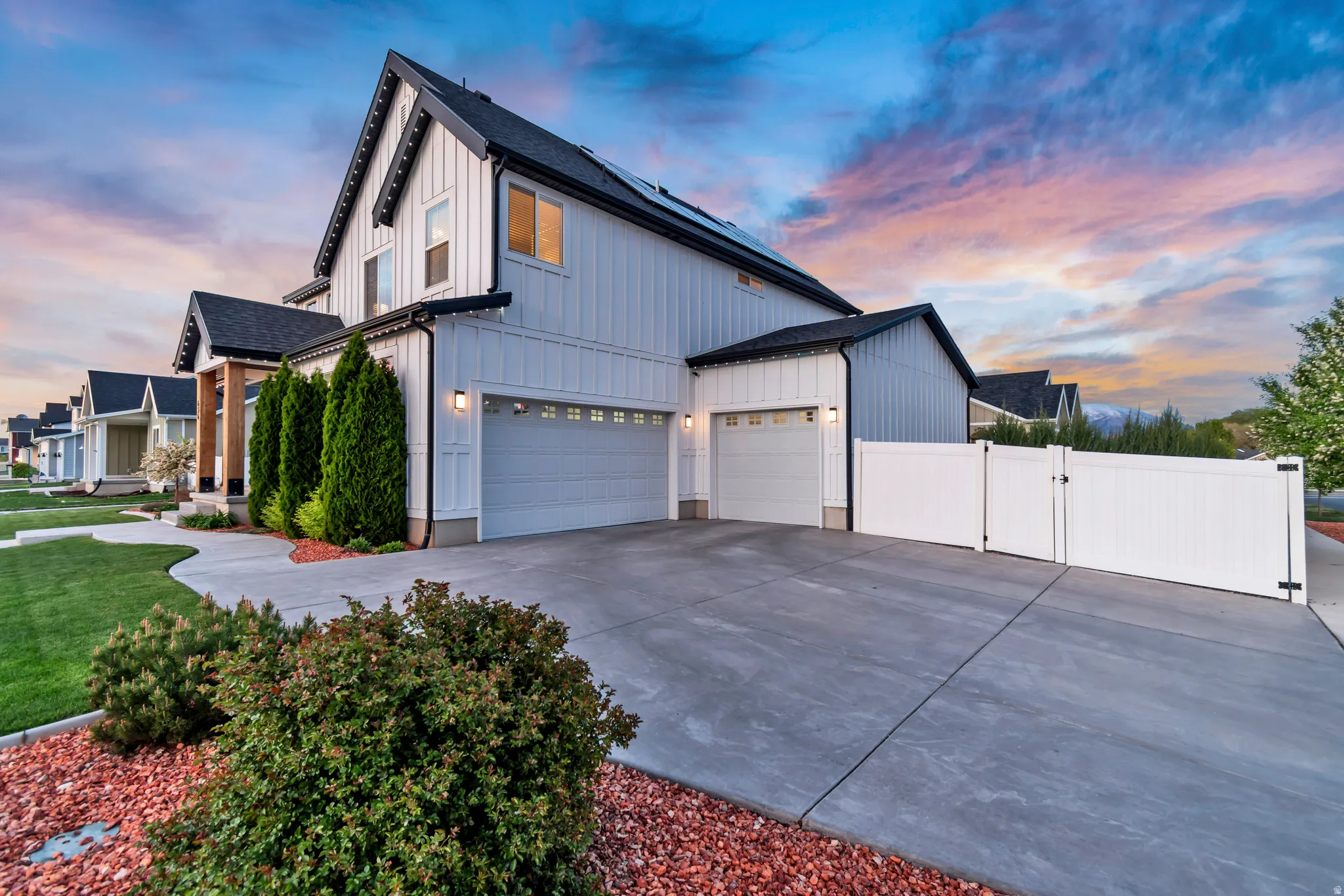 Property exterior at dusk with a gate, concrete driveway, an attached garage, and board and batten siding