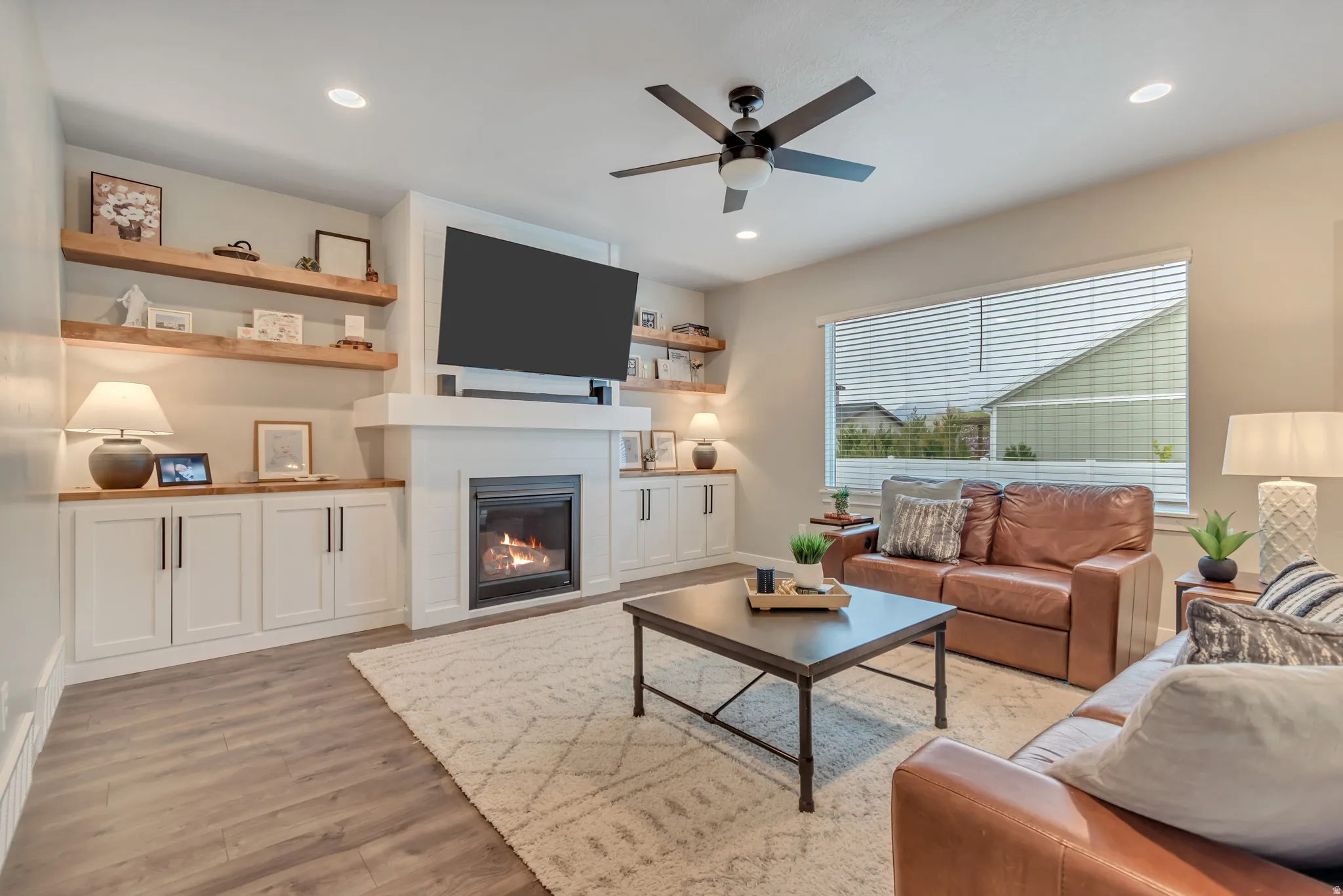 Great room with laminate flooring, cozy fireplace, ceiling fan, and recessed lighting