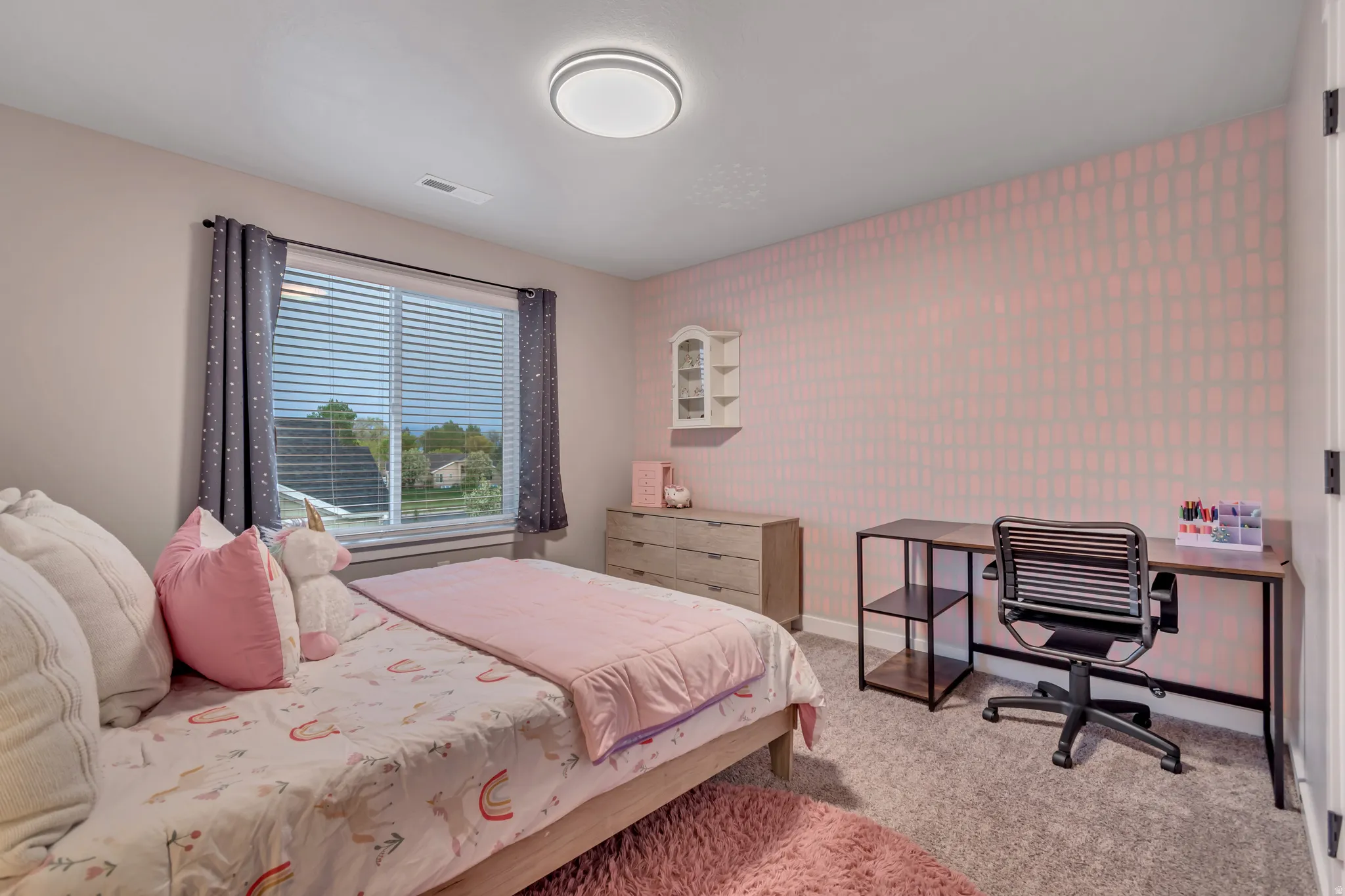 Bedroom with wallpapered walls, light carpet, an office area, and an accent wall