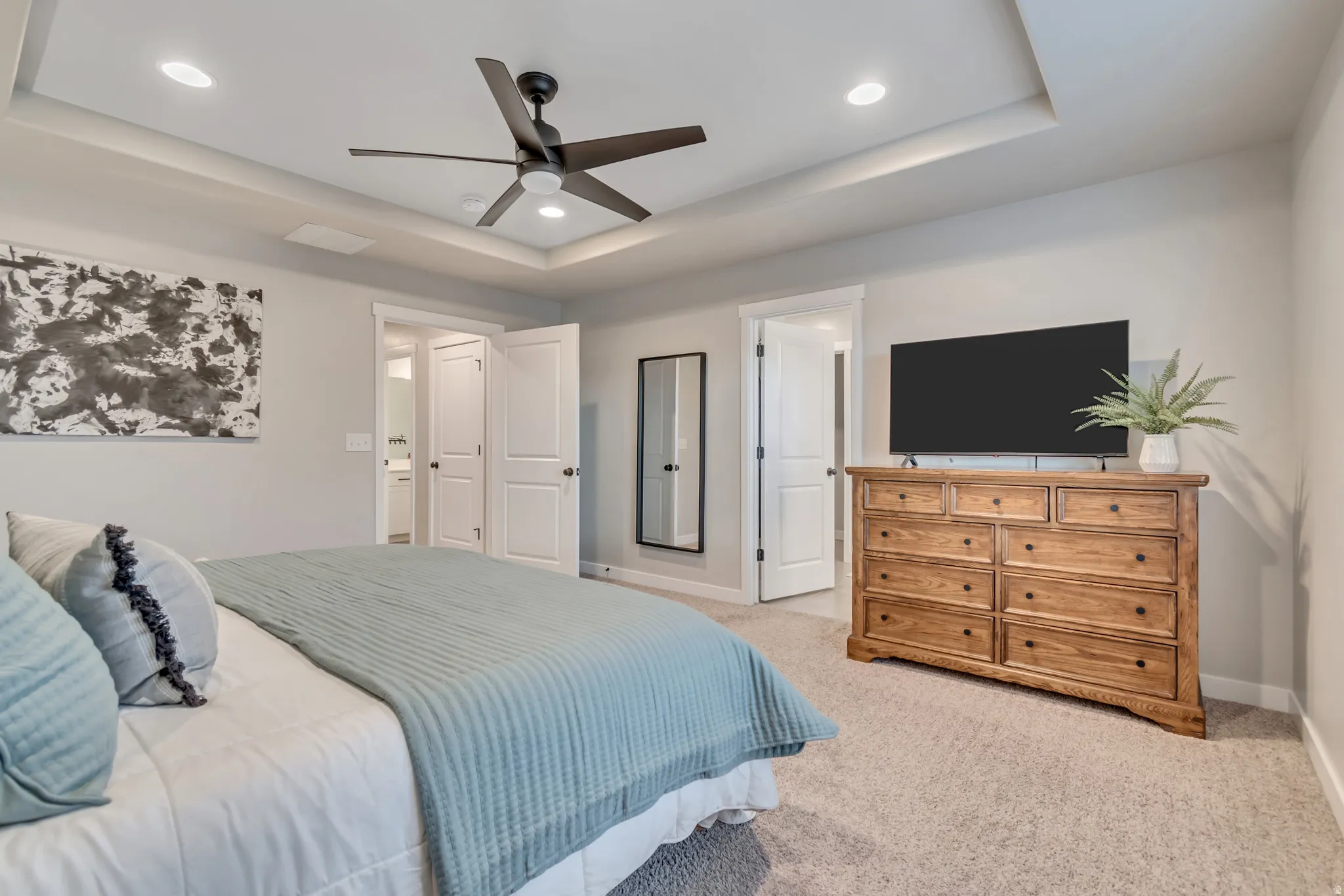Primary bedroom with a tray ceiling, light colored carpet, ceiling fan, and recessed lighting