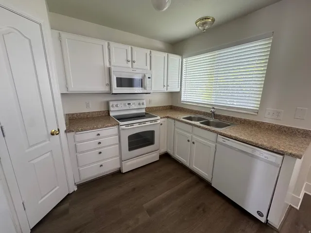 Kitchen with white cabinetry, white appliances, dark wood-style floors, and light countertops