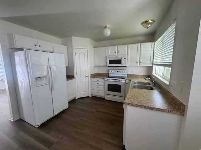 Kitchen with white appliances, white cabinetry, dark wood finished floors, and dark countertops