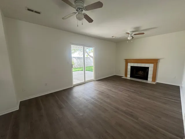 Unfurnished living room with dark wood-style flooring, a ceiling fan, and a fireplace
