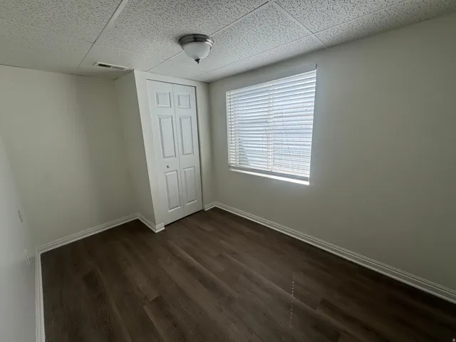 Unfurnished bedroom with dark wood finished floors, a closet, and a paneled ceiling