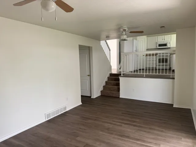 Unfurnished living room featuring a ceiling fan and dark wood-style flooring