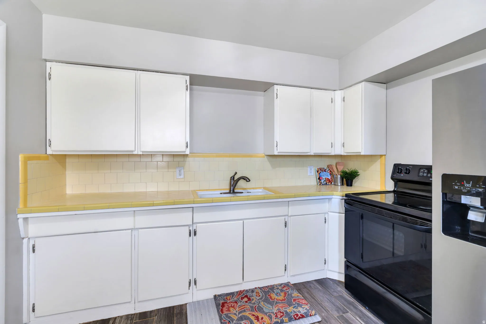 Kitchen with tile counters, black / electric stove, white cabinets, stainless steel refrigerator with ice dispenser, and backsplash