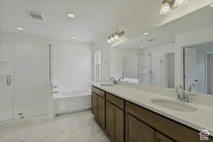 Dual vanity with undermount sinks, full-width mirror, separate shower with glass enclosure, soaking tub, and tile flooring