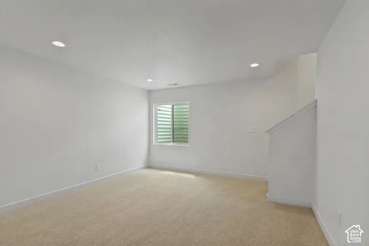 Carpeted interior with recessed lighting, a window, and a staircase with a white railing
