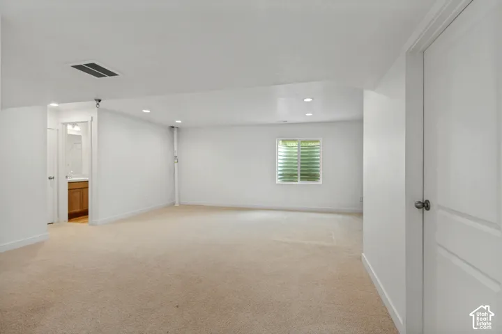 Recessed lighting illuminates a spacious room featuring light-toned carpeting and a window,