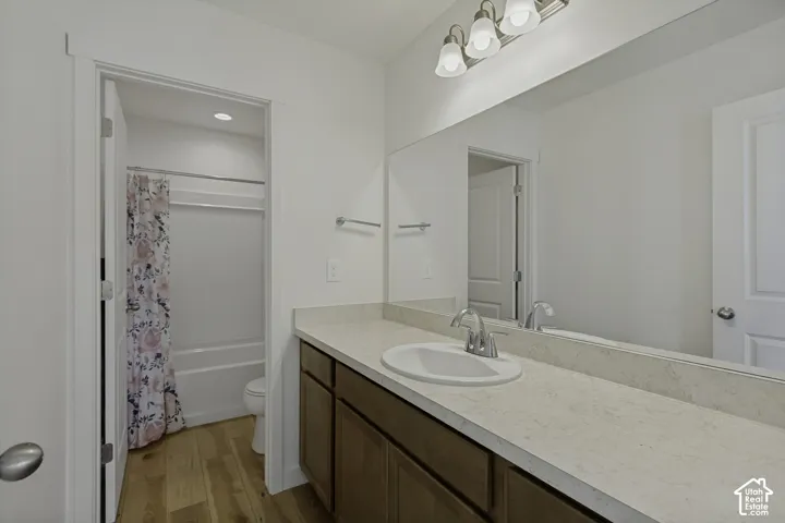 Bathroom featuring a single vanity with tons of counter space, wood-finish cabinetry, a large integrated mirror, a white undermount sink, and a combination tub/shower with a white surround,