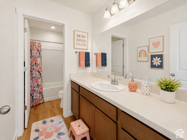 Bathroom featuring a single vanity with tons of counter space, wood-finish cabinetry, a large integrated mirror, a white undermount sink, and a combination tub/shower with a white surround, AI Staged