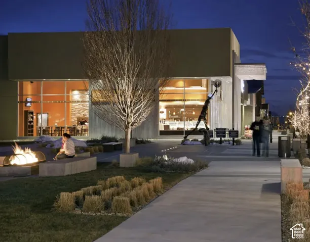 Paved walkway leading to a commercial building with large glass windows, featuring an outdoor fire pit and stone seating