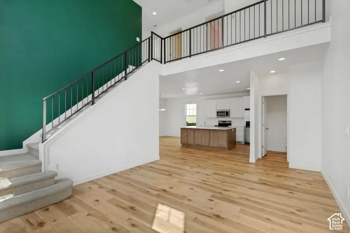Two-story living area featuring wood-finish flooring, a carpeted staircase with metal railings, a kitchen with white cabinetry and stainless steel appliances, and a two-tone kitchen island