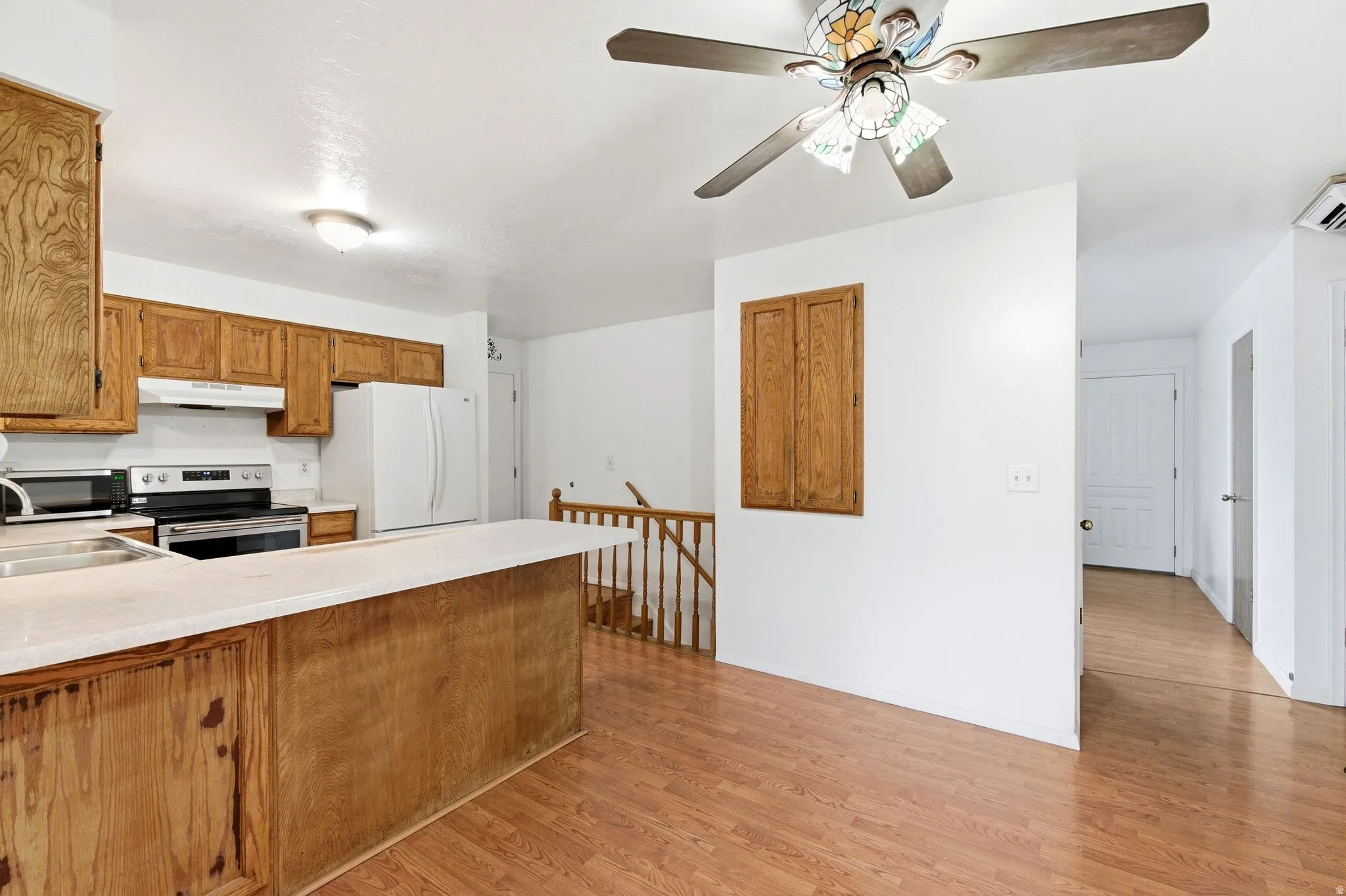 Kitchen featuring light countertops, stainless steel appliances, wood finish cabinetry, light wood-style floors, and a peninsula