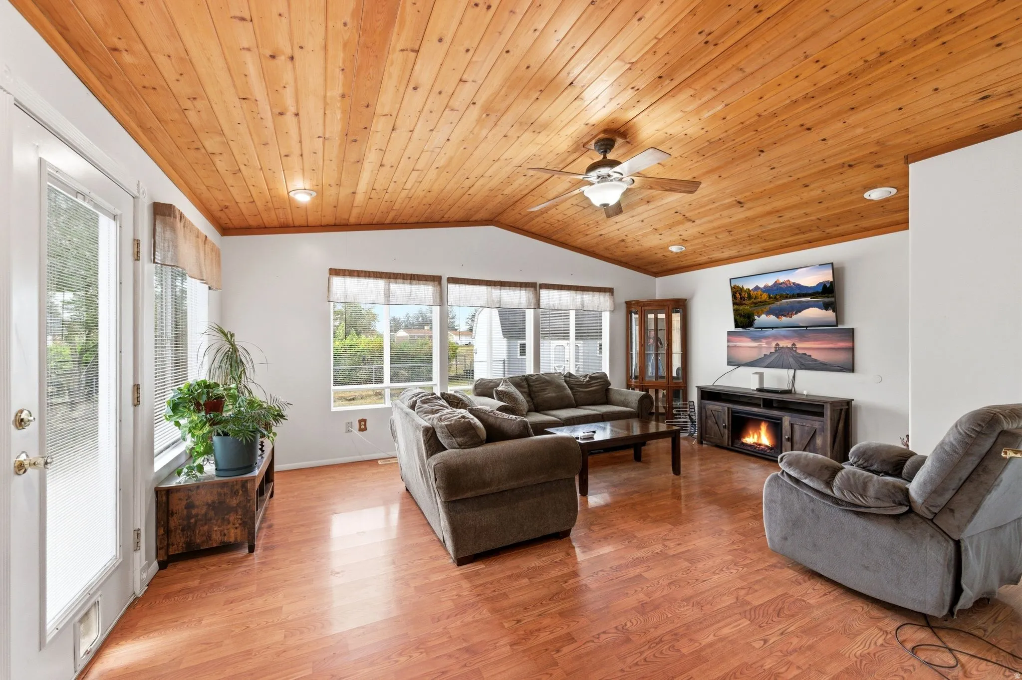 Living area with a glass covered fireplace, wood ceiling, ceiling fan, and light wood-type flooring
